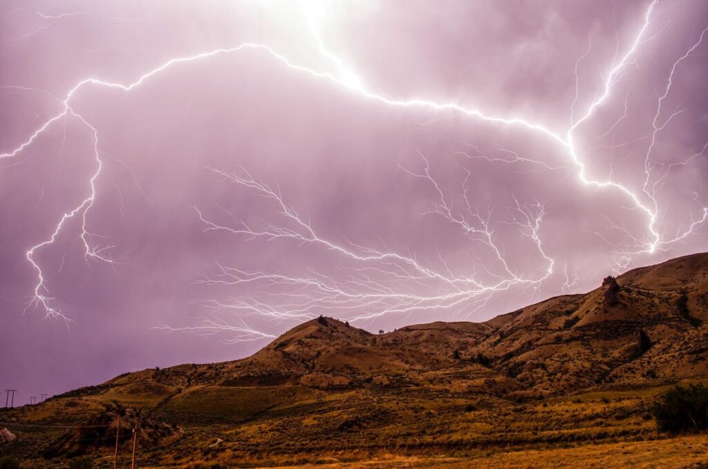 Large lightning strike with a purple sky and brown hills with little vegetation