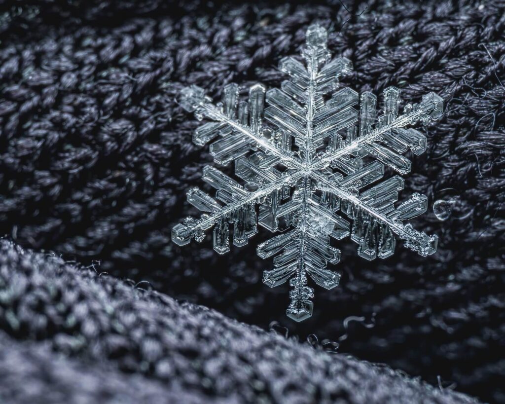 A snowflake laying on a black, woven fabric
