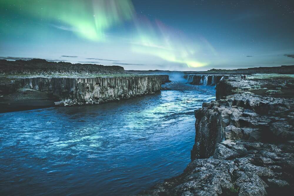 a blue river in a canyon with the aurora borealis in the sky
