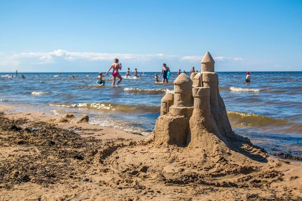 Sandcastle with people behind in the ocean and a blue sky