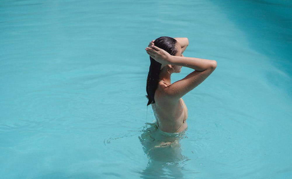 A person with long black hair bathing in blue water