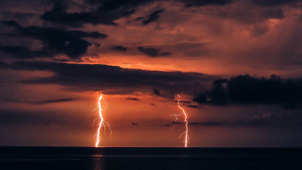 A charge of lightning hitting the water with a red sky and clouds