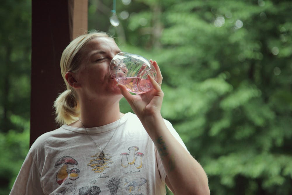 Person drinking water from a glass with green foliage in the background