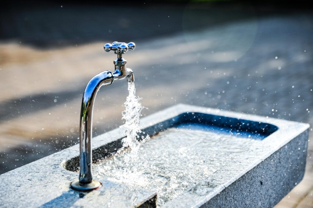 faucet with water flowing onto a solid-stone outdoor, shallow sink.